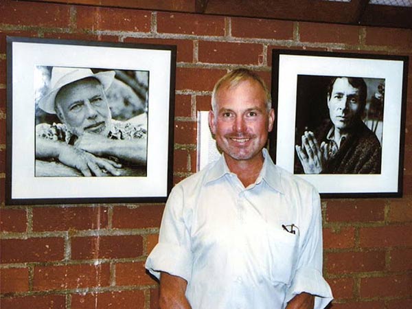 mark thompson standing in front of a brick wall with portraits hanging on it.