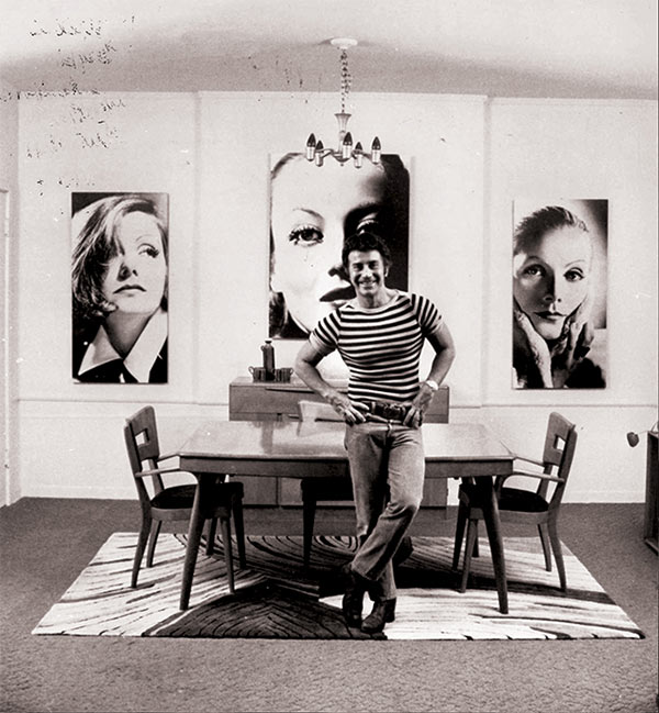 john rechy posing in front of art.